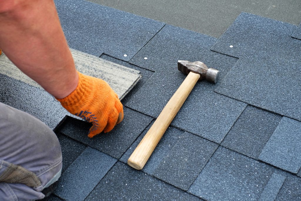 Roof Repair 2 Contractor hands installing bitumen roof shingles using hammer in nails.